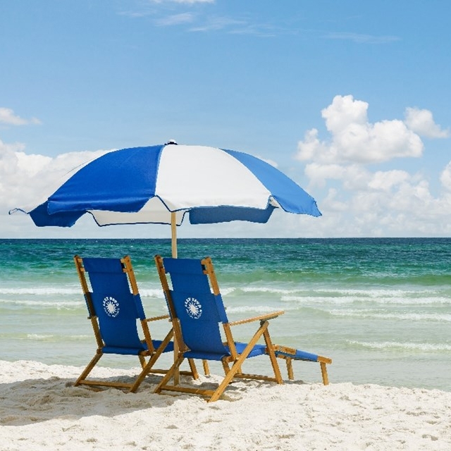 Two blue and white beach chairs under a matching umbrella on a sandy beach with the ocean in the background.