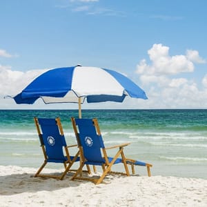 Two blue and white beach chairs under a matching umbrella on a sandy beach with the ocean in the background.