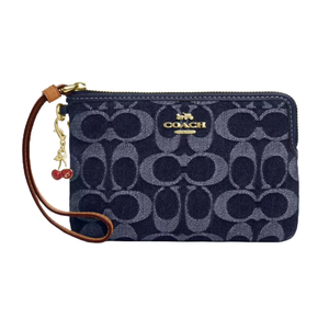 Coach Outlet wristlet in navy with a signature \“C\“ pattern, featuring a gold-tone logo and a brown leather strap adorned with a cherry charm.