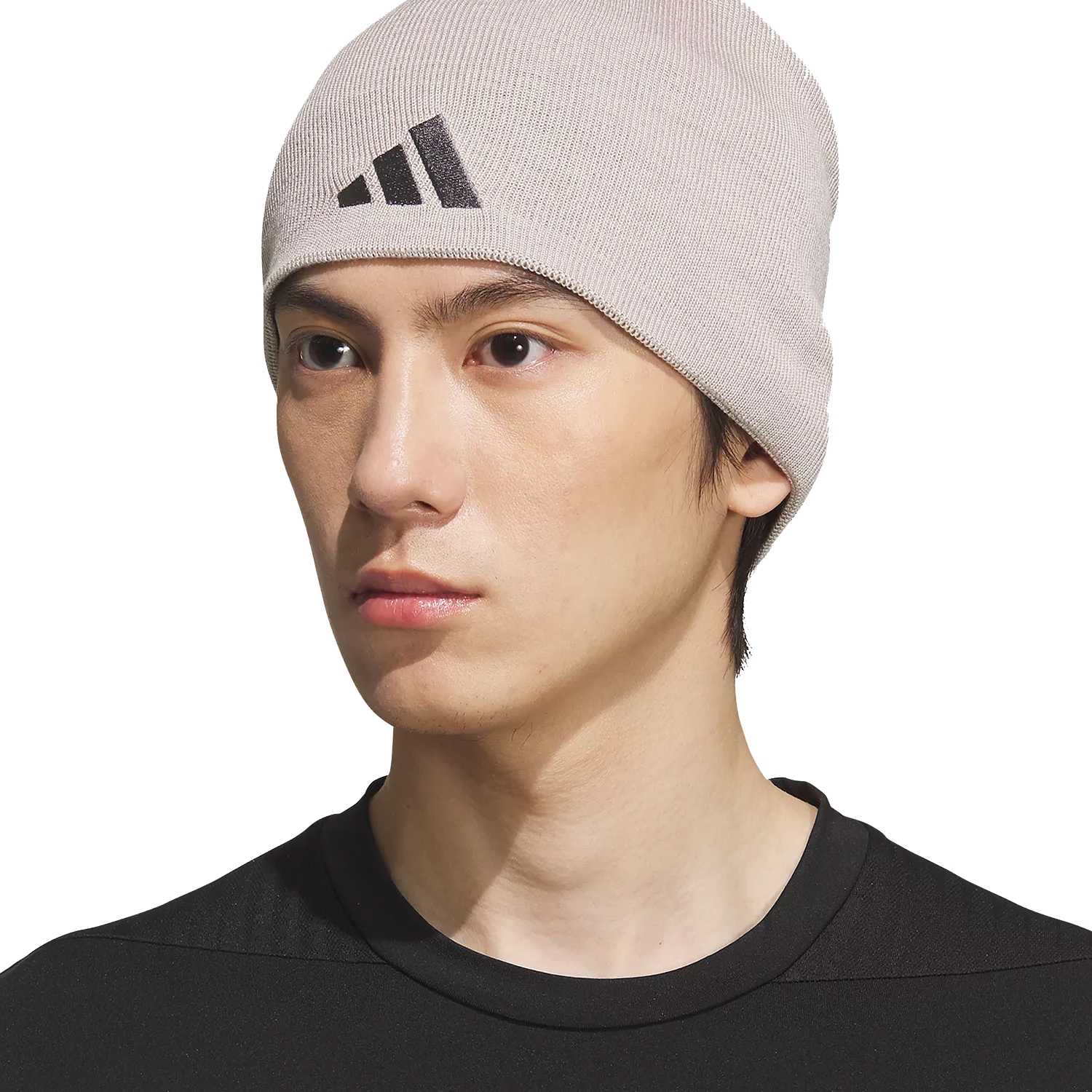 A person wearing a beige Adidas beanie hat with a black logo, paired with a black shirt.