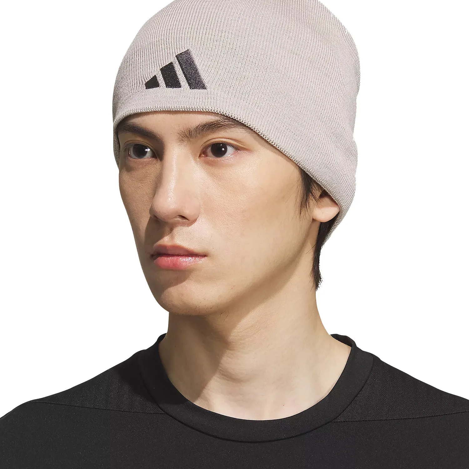 A person wearing a beige Adidas beanie hat with a black logo, paired with a black shirt.