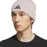 A person wearing a beige Adidas beanie hat with a black logo, paired with a black shirt.