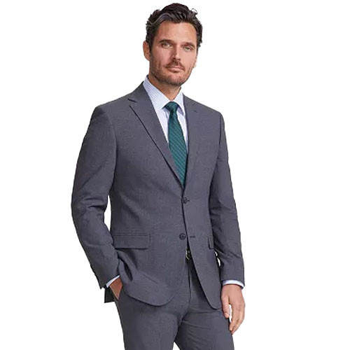 A man wearing a gray two-piece suit, white dress shirt, and teal tie with one hand in his pocket, projecting a formal business attire look.