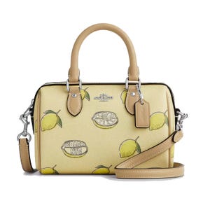 Coach handbag featuring a lemon print design, with beige handles and detachable strap.