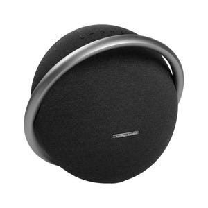 A Harman Kardon wireless speaker with a circular design and a fabric exterior, featuring a metallic handle and control buttons on top.