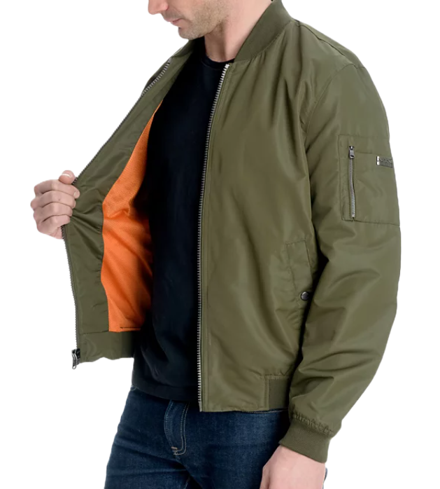 A man is wearing a green Michael Kors bomber jacket with a ribbed collar, cuffs, and hem, featuring a zippered sleeve pocket.