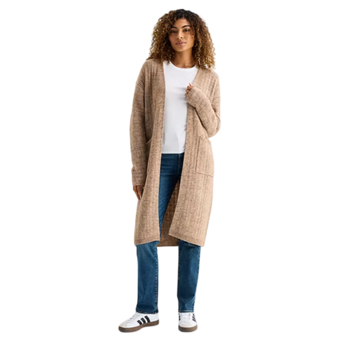 A woman is wearing a long beige knit cardigan over a white T-shirt, paired with blue jeans and white sneakers with black stripes.