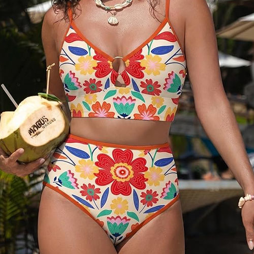 A woman is wearing a colorful floral high-waisted bikini with a keyhole design at the top. She is holding a coconut drink engraved with \“Andicus Premium.\“