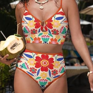 A woman is wearing a colorful floral high-waisted bikini with a keyhole design at the top. She is holding a coconut drink engraved with \“Andicus Premium.\“