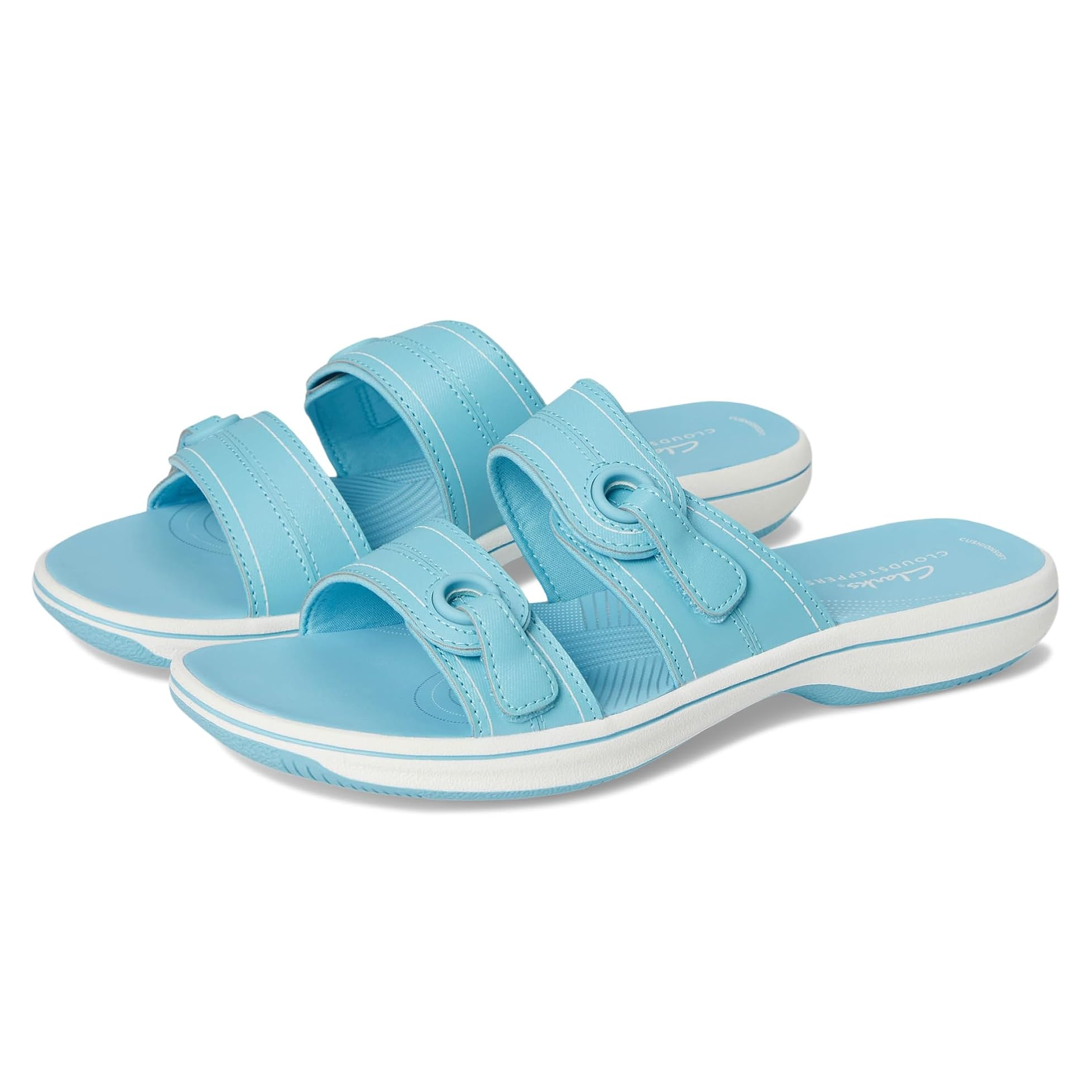 Clarks Breeze Maye Comfort Sandals in light blue feature adjustable straps with decorative stitching and grommet details. They have a cushioned sole for comfort and a slip-on design with a white outsole.