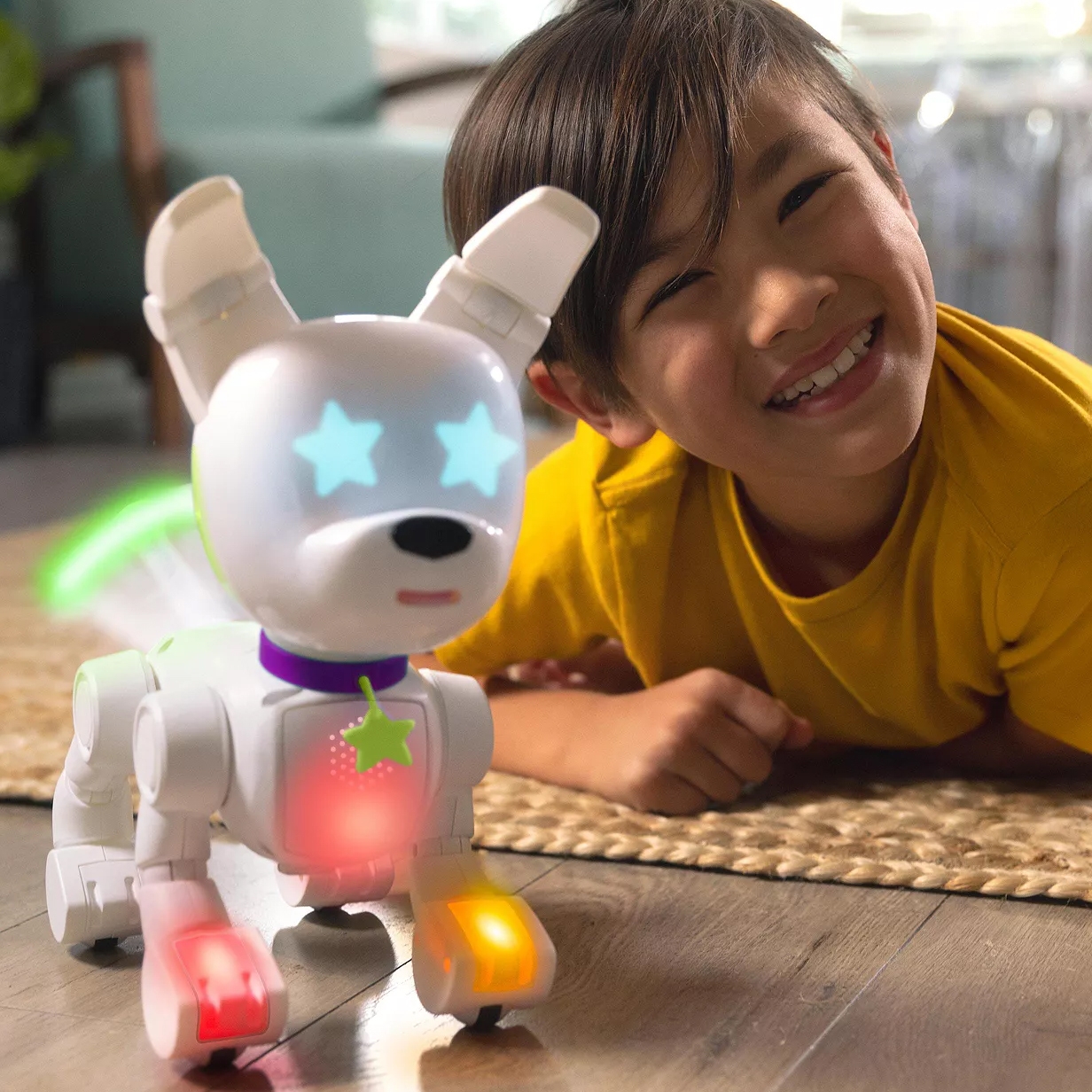 A child in a yellow shirt is playing on the floor with an interactive robotic dog featuring illuminated eyes, paws, and collar.