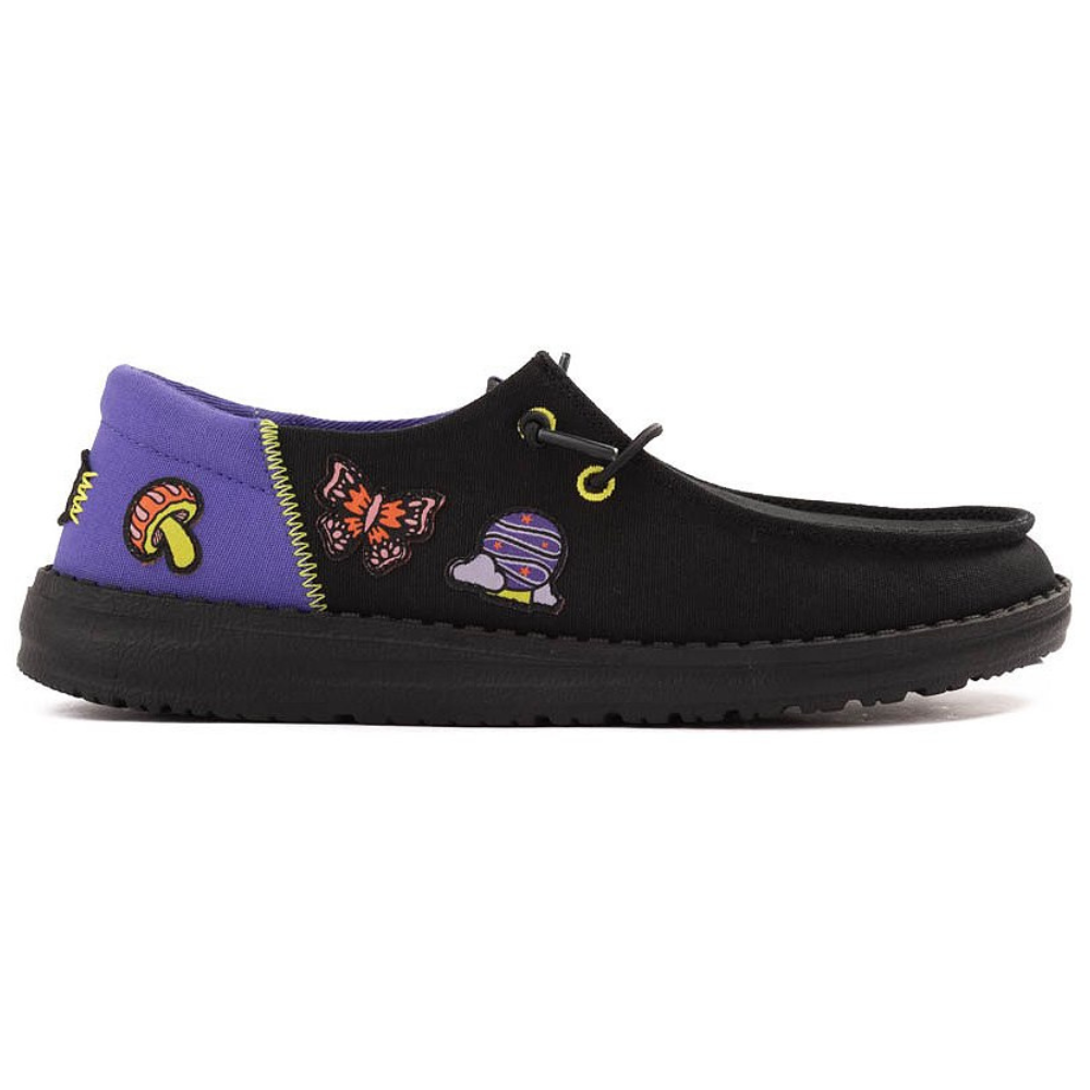 A black slip-on shoe featuring colorful patches, including a mushroom, butterfly, and a space-themed design, with a purple heel accent and black sole.