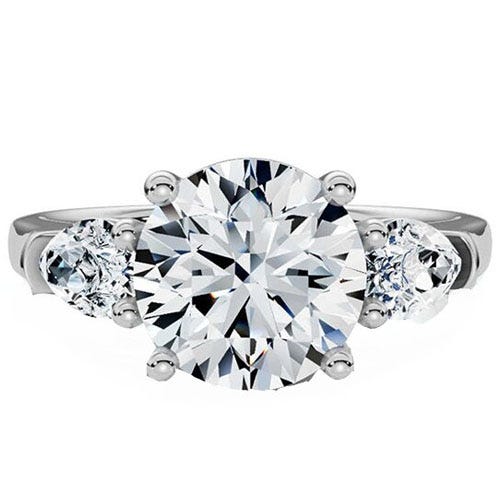 A three-stone engagement ring featuring a large round center diamond flanked by two smaller round diamonds, set in a white metal band.