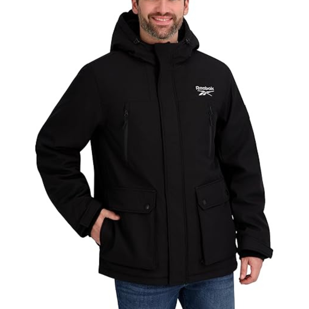 A man is wearing a black Reebok hooded jacket with multiple pockets, paired with blue jeans.
