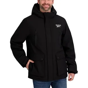 A man is wearing a black Reebok hooded jacket with multiple pockets, paired with blue jeans.