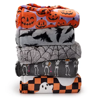 A stack of five plush throw blankets with Halloween-themed patterns, including pumpkins, bats, spider webs, skeletons, and ghosts, in a color scheme of orange, grey, white, and black.