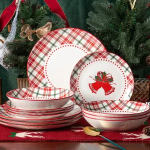 Festive dinnerware set featuring plates and bowls adorned with red and green plaid patterns and Christmas bell designs, set on a holiday-themed table with decorative fir branches and ribbon accents.