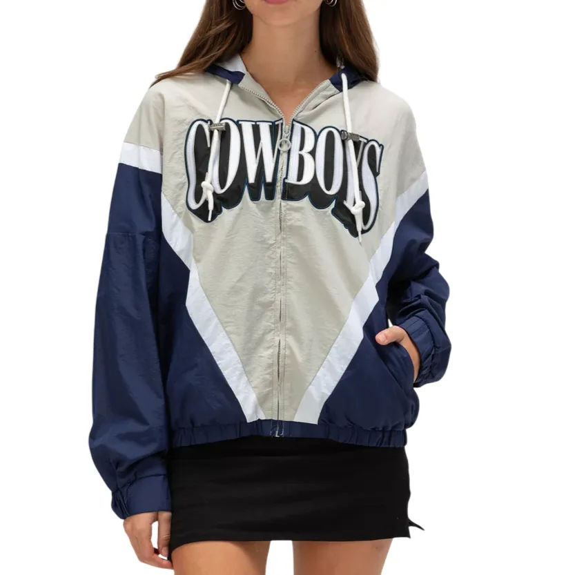 A woman models a color-blocked windbreaker with \“COWBOYS\“ printed on the front, featuring a mix of navy, gray, and white, with a zip closure and drawstring hood.