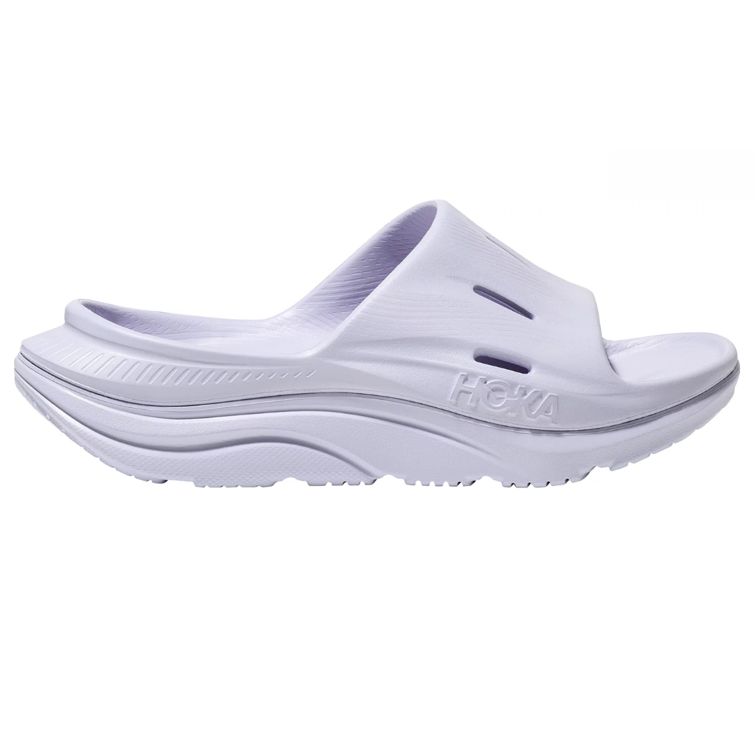Hoka Ora Recovery Slides are white, open-toe slip-ons with a thick, cushioned sole for comfort and support. They feature ventilation slots and the Hoka logo on the side.