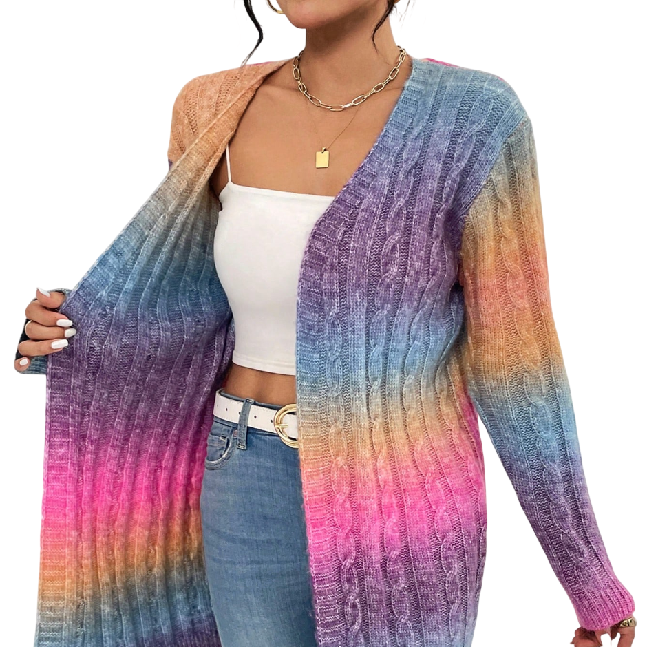 A person wears a long, gradient-colored cable knit cardigan with shades of orange, blue, purple, and pink, paired with a white top and blue jeans. Accessories include a gold chain necklace and a white belt.