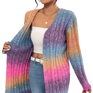 A person wears a long, gradient-colored cable knit cardigan with shades of orange, blue, purple, and pink, paired with a white top and blue jeans. Accessories include a gold chain necklace and a white belt.