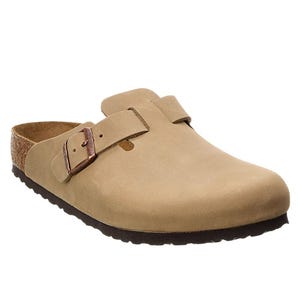 A tan slip-on clog with a brown buckle strap and cork footbed, featuring a black textured sole for traction.