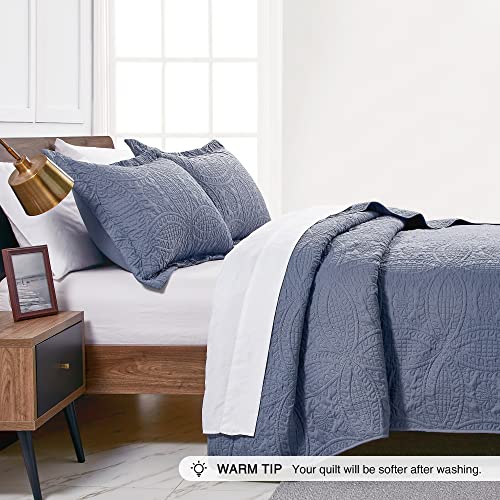 A queen-size quilt in a solid dark blue with intricate stitched patterns, accompanied by two matching pillow shams.
