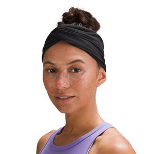 A person wearing a black twisted headband and a purple athletic tank top.