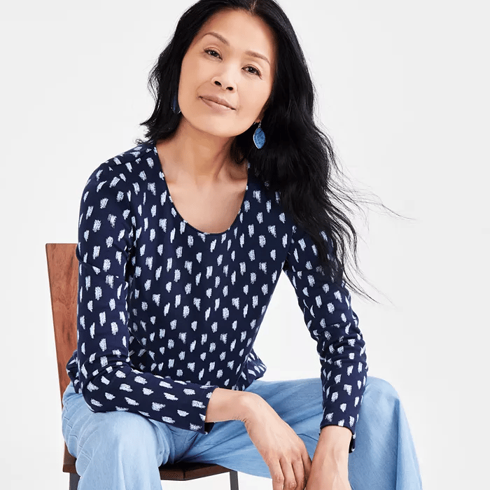 A woman is wearing a navy blue printed top, light blue jeans, and teal drop-shaped earrings.