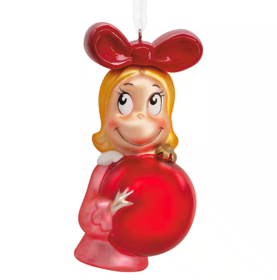 A Christmas ornament depicting a smiling character with blonde hair, a large red bow, and a red dress holding a shiny red ornament ball.