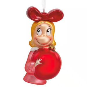 A Christmas ornament depicting a smiling character with blonde hair, a large red bow, and a red dress holding a shiny red ornament ball.