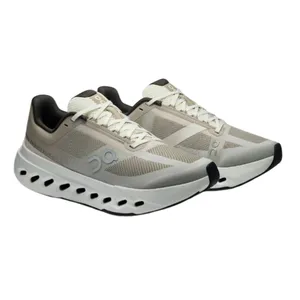 Athletic shoes with a beige and black color scheme, featuring mesh panels, lace-up closure, and a distinctive sole with circular cutouts for ventilation.