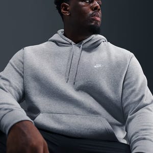 A person wearing a gray Nike hoodie featuring the brand's logo on the chest, with a drawstring hood and a front pocket.