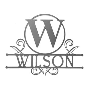 A decorative metal sign featuring the letter \“W\“ inside a circle and the name \“Wilson\“ in stylized font, embellished with ornamental flourishes.
