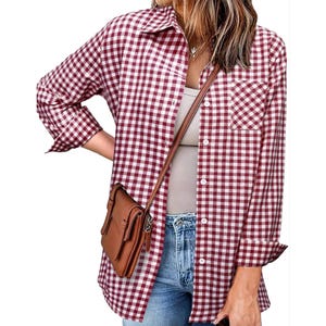 A woman wears a checkered red and white button-up shirt over a beige tank top, paired with jeans and a brown crossbody bag.