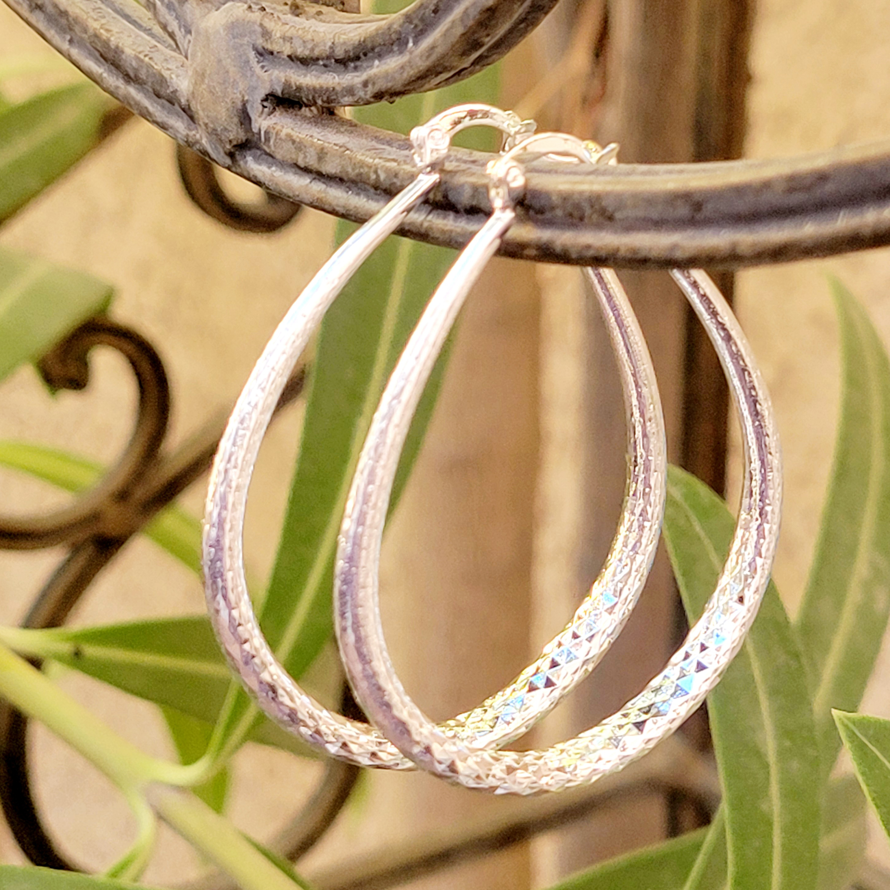 Silver textured hoop earrings hanging on a metal railing with a natural background.