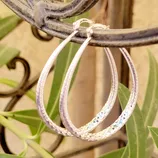 Silver textured hoop earrings hanging on a metal railing with a natural background.