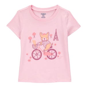 Pink toddler girls' T-shirt featuring a cute dog riding a bicycle, with a basket holding bread and an Eiffel Tower illustration in the background, embellished with flowers and trees.