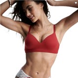 A woman is wearing a red wireless bra and lace-trimmed underwear, smiling with her arms raised. She's accessorized with a delicate necklace.