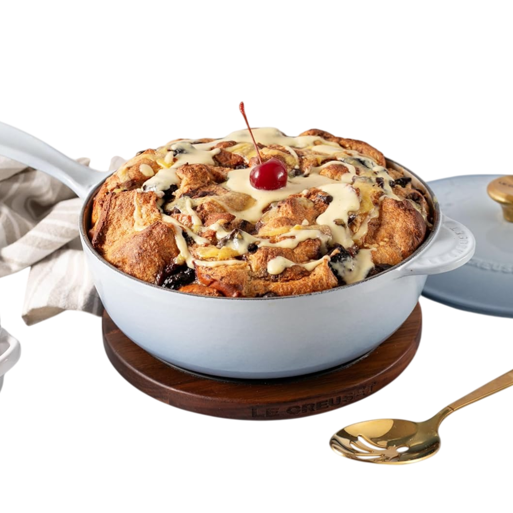Bread pudding topped with a cherry and sauce in a Le Creuset pan, with additional cherries and sauce in separate bowls nearby.