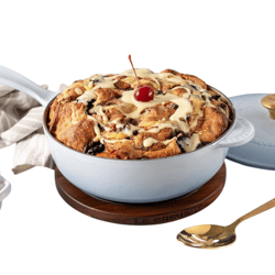 Bread pudding topped with a cherry and sauce in a Le Creuset pan, with additional cherries and sauce in separate bowls nearby.