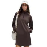 A woman is wearing a brown long-sleeve dress with a zip-up collar, a white bag slung over her shoulder, and a white cap.