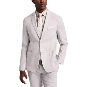 A man wears a light gray pinstripe suit with a beige shirt and striped tie. The suit features a notch lapel and patch pockets.