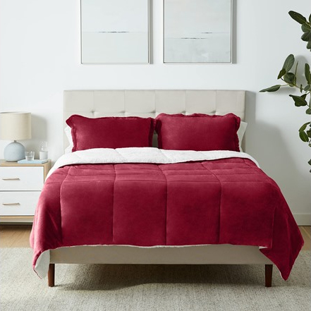 A bed with a red velvet comforter set and white headboard, flanked by white nightstands and wall art.