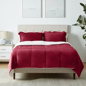 A bed with a red velvet comforter set and white headboard, flanked by white nightstands and wall art.