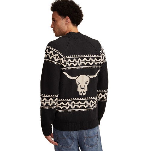 A man is wearing a black sweater featuring a white longhorn skull design and geometric patterns.