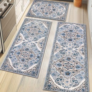 Three blue and white patterned kitchen rugs with intricate designs are placed on a light wooden floor in front of kitchen cabinets and an oven.