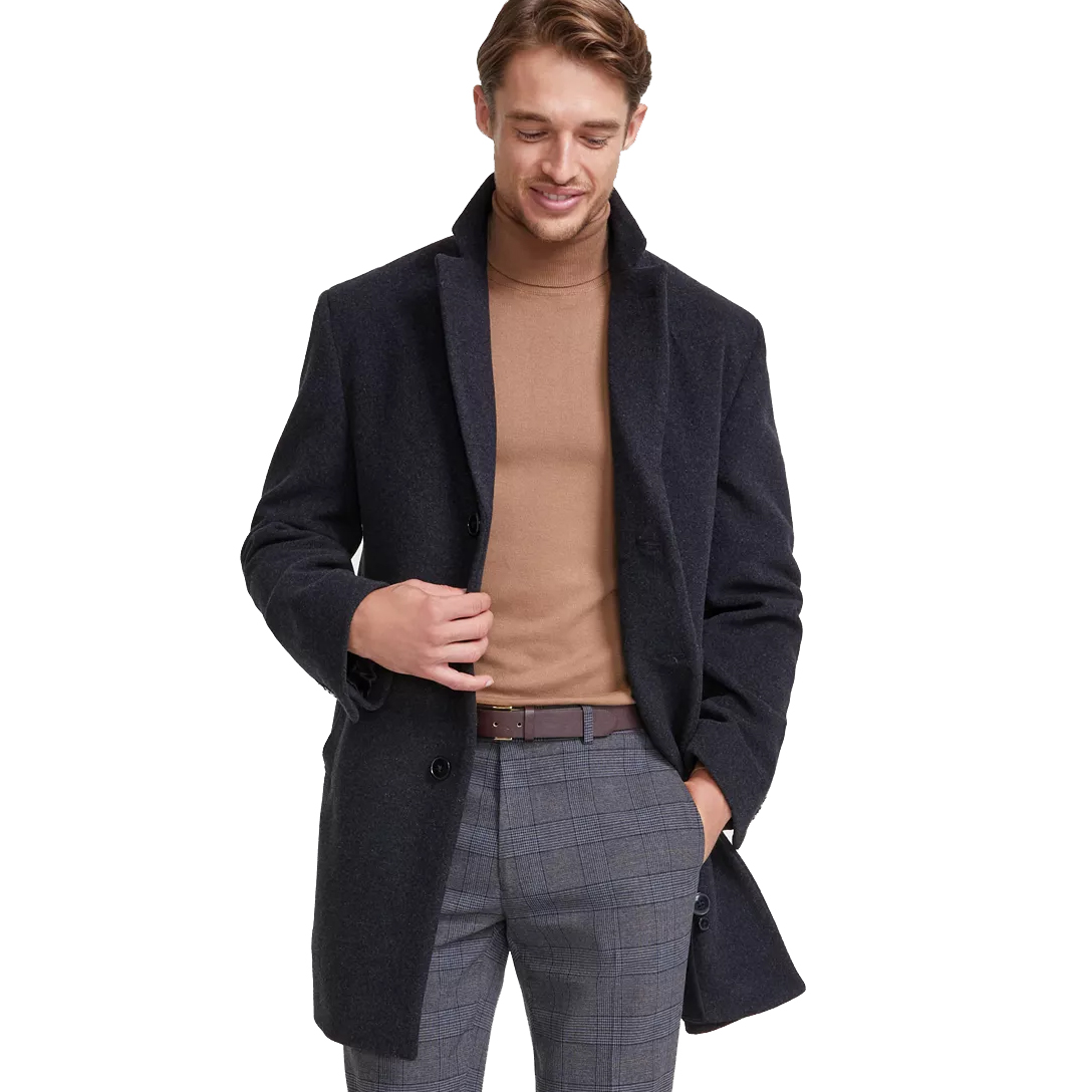 A man is wearing a dark overcoat, a light brown turtleneck, and gray plaid trousers, accessorized with a brown belt.