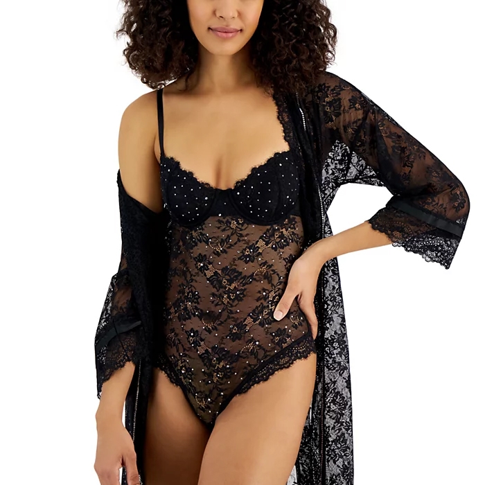 A woman is wearing a black lace bodysuit with dotted details and a matching sheer lace robe with wide sleeves.