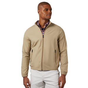 A man wearing a beige zip-up jacket over a plaid shirt, paired with white pants.